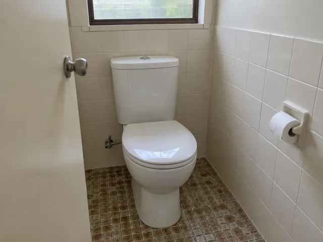 Clean white toilet in a small tiled bathroom with a window and toilet paper holder in Rooty Hill