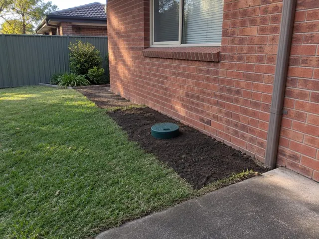Capped sewer access beside a brick house with freshly reinstated soil strip and lawn in Doonside